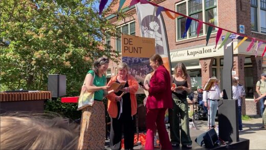 Een groep vrouwen op een podium. Karin Verdooren van Lieven de Key heeft het eerste exemplaar van een boekje over De Punt uitgereikt aan buurtactiviste Eva Bollen.